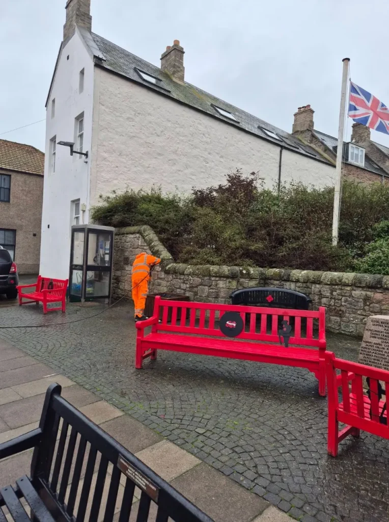 Freshly washed red benches in the town centre, with a volunteer in hi-vis in the distance