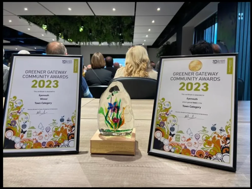 Two framed Greener Gateway Community Awards 2023 certificates and a glass trophy on a table